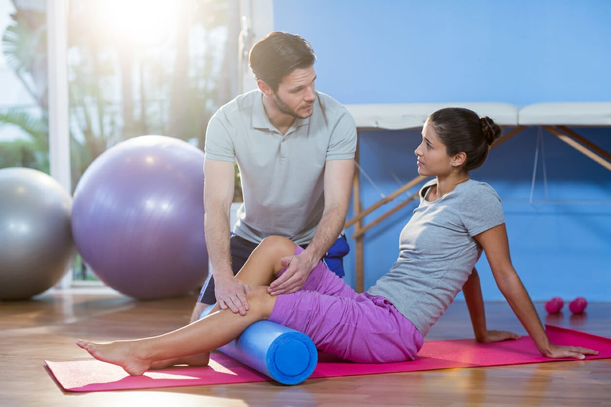 Physiotherapist assisting woman while exercising on exercise mat