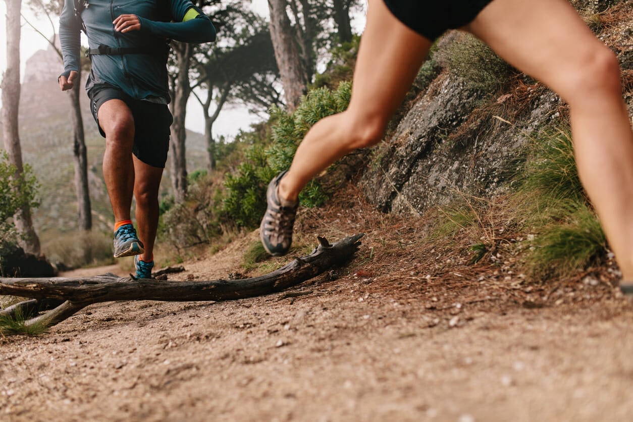 Healthy young couple trail running running on mountain trail in morning. Young man and woman jogging on country path, focus on legs.