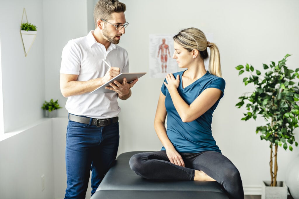 A Modern rehabilitation physiotherapy man at work with woman client talk about shoulder problem – Mountain Land – Mountain Land Physical Therapist assess patient