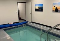 Indoor shallow pool in a rehabilitation or recreation facility, with a metal handrail and wall-mounted photos on the beige walls.