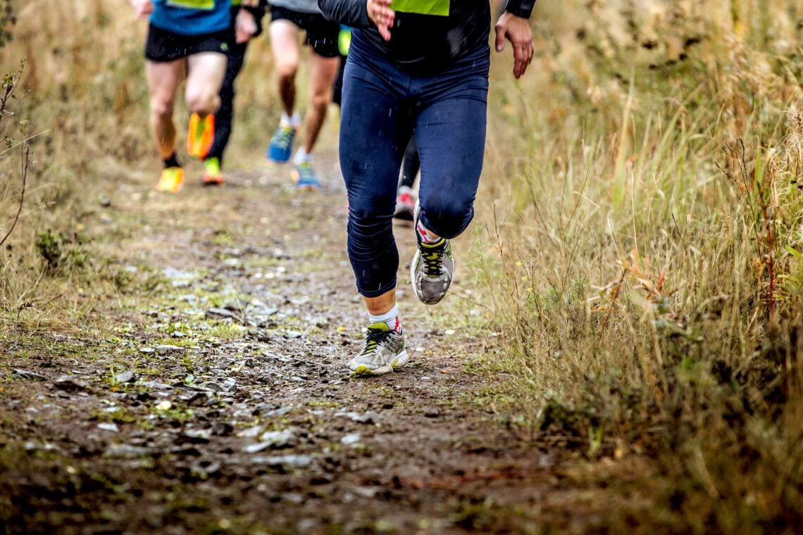 group runners running uphill in autumn trail of mud and stones