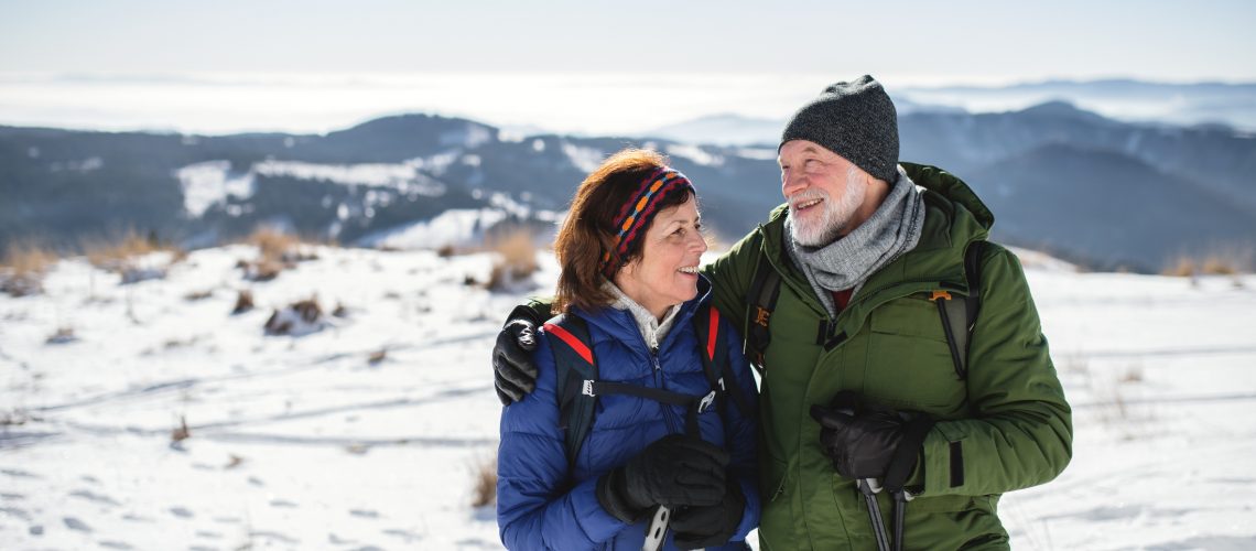 Senior couple hikers with nordic walking poles in snow-covered winter nature