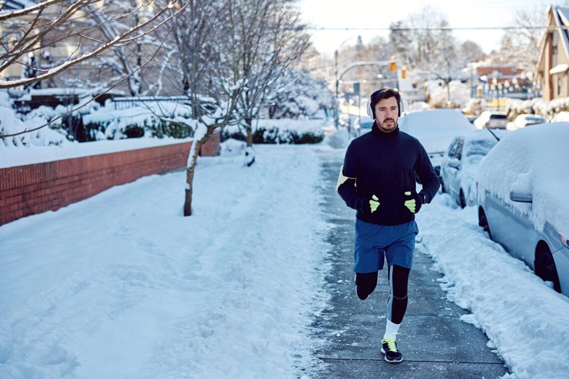 Motivated sportsman running on the street during snowy day. Copy space.